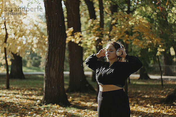 Junge Frau mit geschlossenen Augen genießt Musik und hört im Park über kabellose Kopfhörer