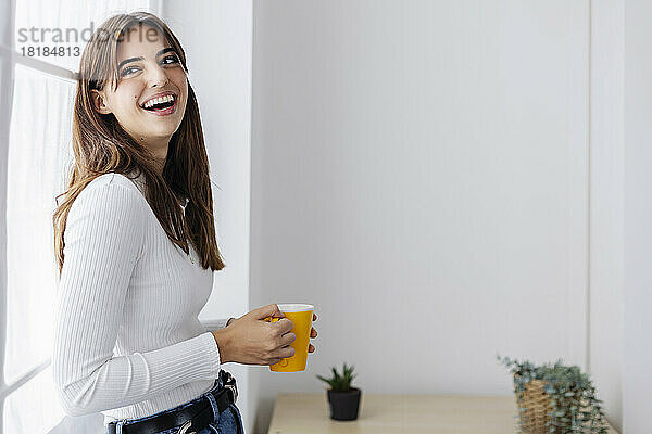 Schöne Frau hält Kaffeetasse und lacht zu Hause