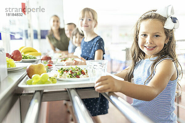 Smiling schoolgirl with fruits and food on tray at lunch break