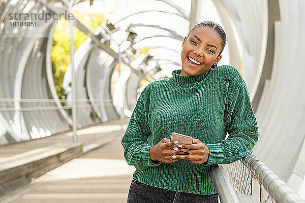 Glückliche junge Frau hält Mobiltelefon auf Brücke