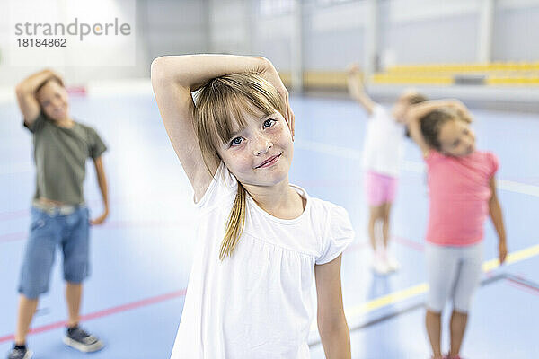 Smiling girl with bangs stretching neck with friends at school sports court