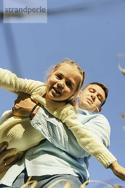 Glücklicher Mann spielt mit Tochter unter blauem Himmel