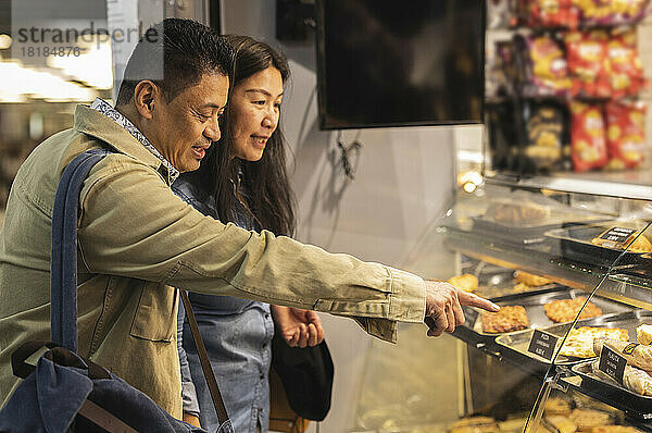 Älteres Paar beim Einkaufen zeigt auf Lebensmittel  die in der Bäckerei ausgestellt sind