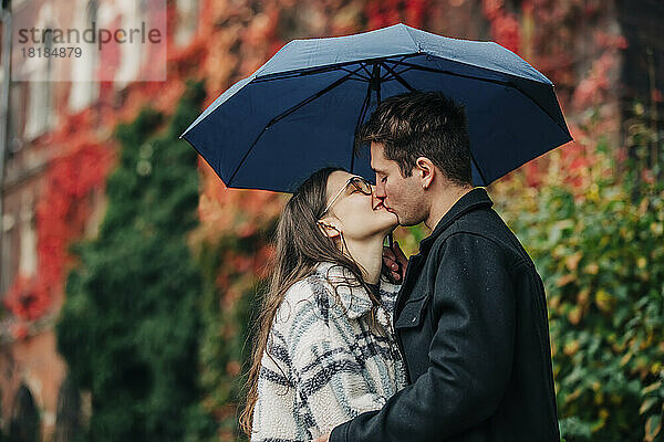 Young couple kissing on mouth under umbrella