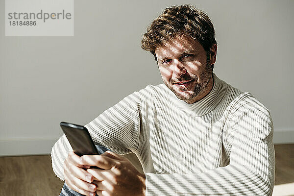 Lächelnder  gutaussehender Geschäftsmann mit Smartphone im Büro
