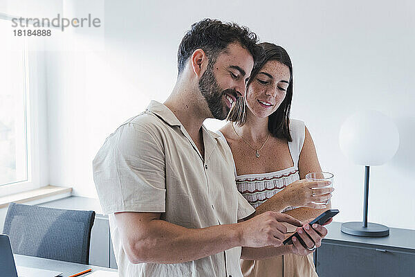 Lächelnder Geschäftsmann teilt Smartphone mit Geschäftsfrau im Büro