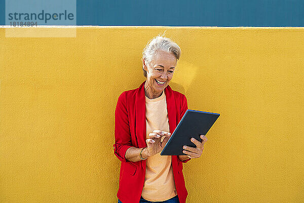 Glückliche reife Frau mit rotem Blazer mit Tablet-PC