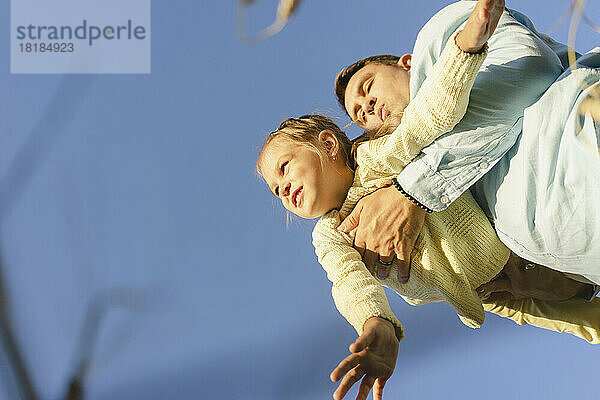 Glücklicher Mann  der an einem sonnigen Tag mit seiner Tochter unter blauem Himmel spielt