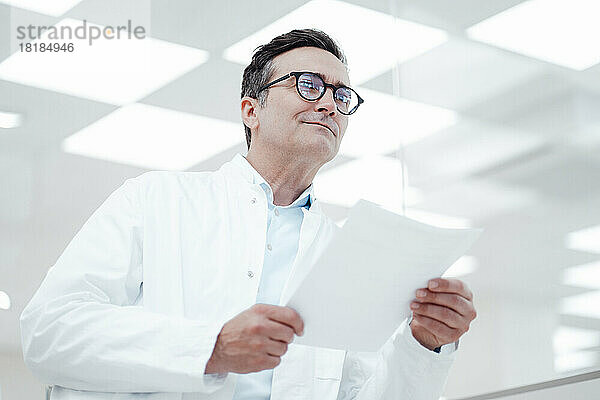 Nachdenklicher Mann im Laborkittel hält Dokument im Labor