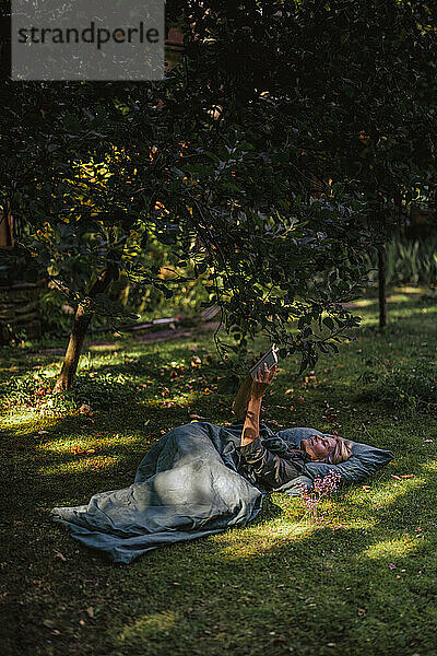 Frau liegt auf Gras und liest Buch im Garten