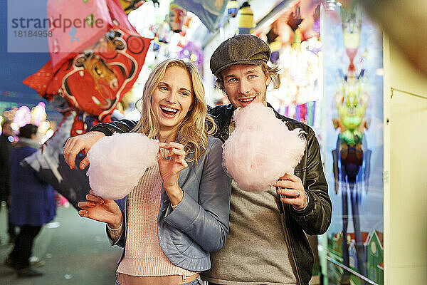 Young couple at fun fair eating candy floss