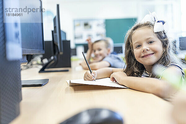 Smiling girl with book and pencil sitting at desk in classroom