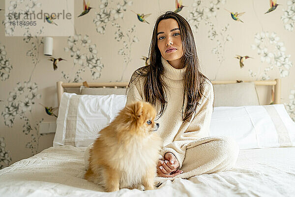 Schöne junge Frau sitzt mit Hund auf dem Bett