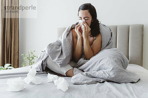 Kranke Frau mit geschlossenen Augen  die zu Hause im Bett die Nase in Taschentuch putzt