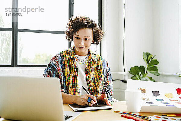 Lächelnder Illustrator mit Grafiktablett und Laptop im Büro