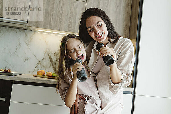 Glückliche Mutter und Tochter singen zu Hause in Pfeffermühlen