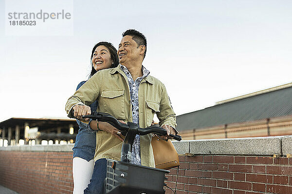 Lächelndes älteres Paar auf Elektrofahrrad vor dem Himmel