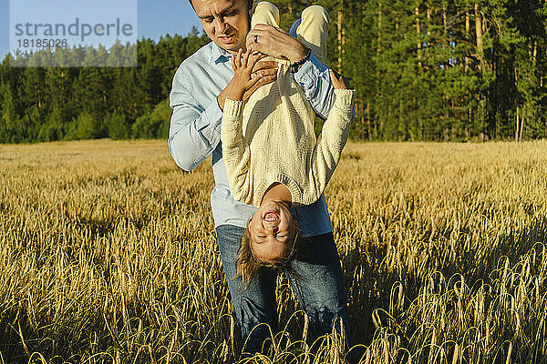 Verspielter Mann trägt glückliche Tochter kopfüber auf dem Feld
