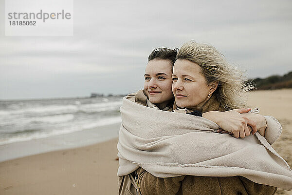 Mother and daughter wrapped in blanket at beach