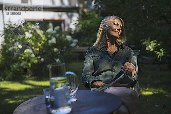 Mature woman with book sitting on chair in garden