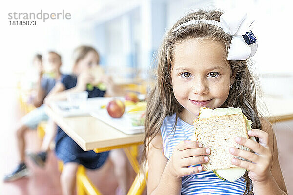 Mädchen mit Stirnband hält Sandwich in der Mittagspause in der Cafeteria
