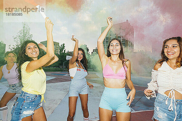 Lächelnde Frau mit Rauchfackel steht mit Freunden am Sportplatz