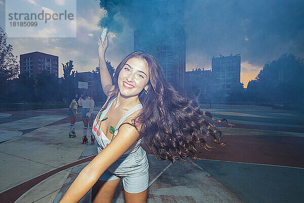 Glückliche junge Frau spielt mit Rauchfackel auf dem Sportplatz