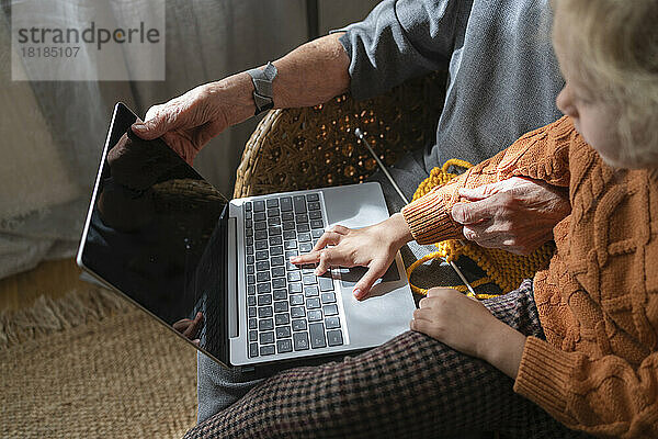 Girl using laptop sitting by grandmother on chair