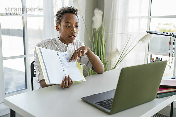 Junge zeigt zu Hause Notizen vor Laptop