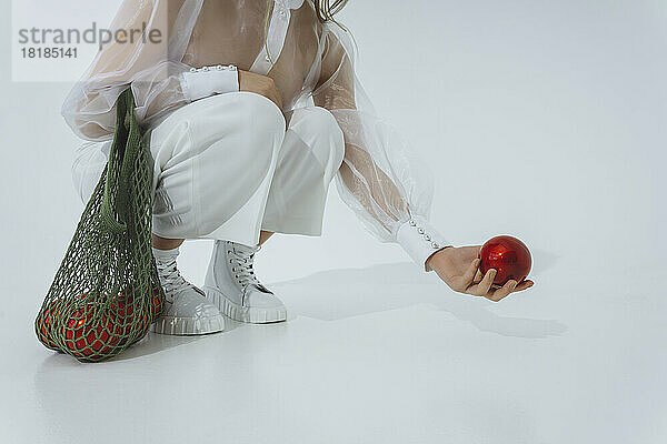 Teenage girl with mesh bag holding Christmas ornament against white background