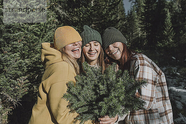 Frauen lachen und bedecken die Augen mit Strickmützen im Wald