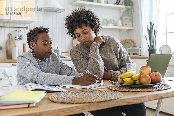 Junge macht Hausaufgaben  Mutter sitzt zu Hause am Tisch