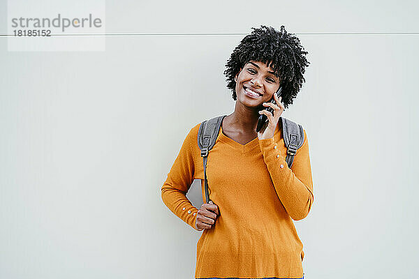 Lächelnde Frau  die vor einer weißen Wand mit dem Mobiltelefon spricht
