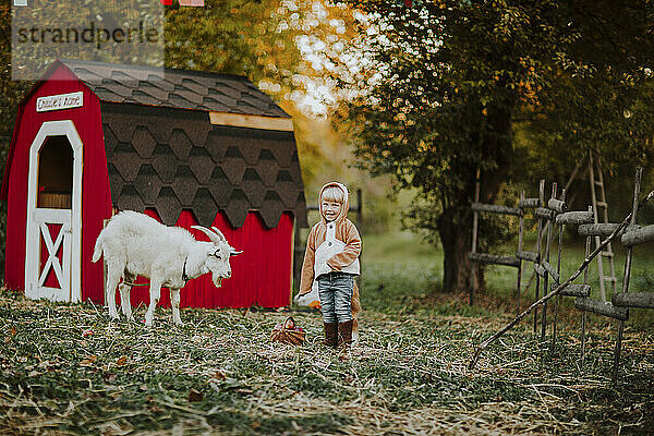 Glückliches Mädchen im Fuchskostüm  das neben der Ziege auf dem Bauernhof steht