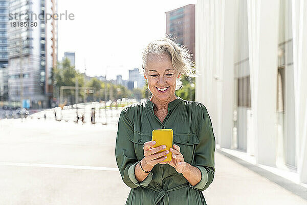 Lächelnde reife Frau  die an einem sonnigen Tag ihr Mobiltelefon benutzt