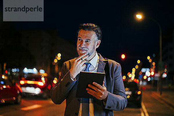 Nachdenklicher reifer Geschäftsmann steht mit Tablet-PC auf der Straße