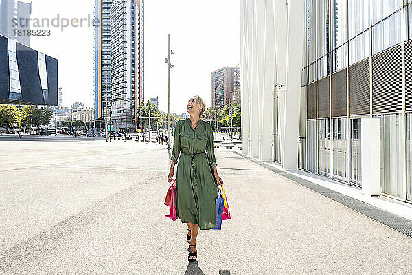 Reife Frau mit Einkaufstüten lacht auf Fußweg in der Stadt