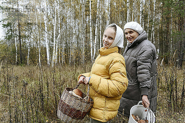 Lächelndes Mädchen mit Großmutter beim Pilzesammeln im Wald