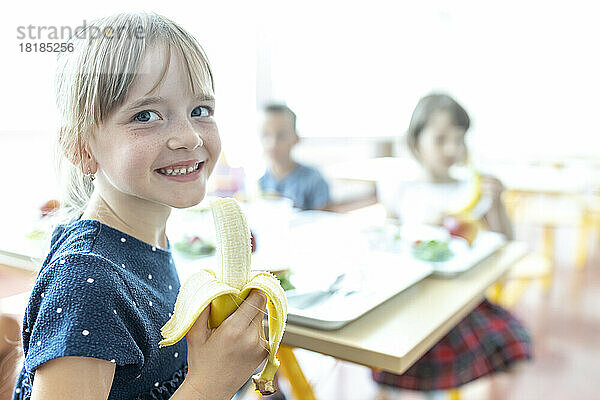 Smiling girl holding banana at lunch break in cafeteria
