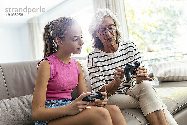 Großmutter zeigt Enkelin  die zu Hause auf dem Sofa sitzt  den Gamecontroller