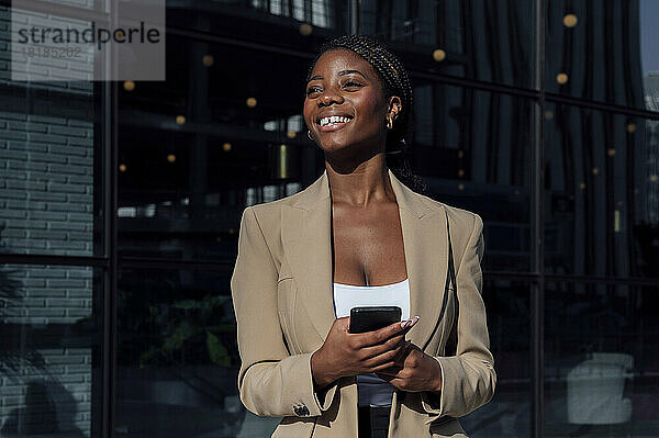 Glückliche Geschäftsfrau  die an einem sonnigen Tag mit ihrem Smartphone steht