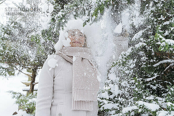 Frau steht unter fallendem Pulverschnee neben einem Baum