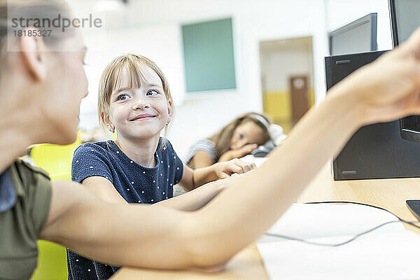 Smiling girl looking at teacher teaching in E-learning class