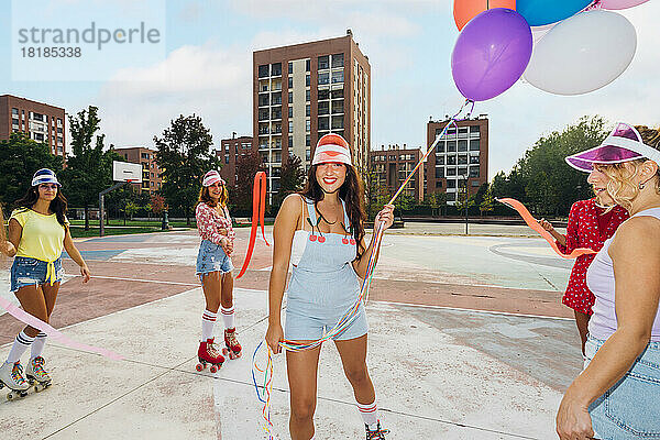 Lächelnde Frau mit Luftballons steht inmitten von Freunden mit Schleife am Sportplatz