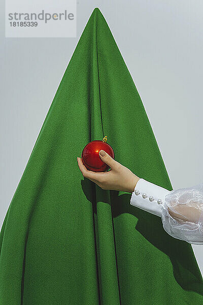 Teenager-Mädchen hält rote Verzierung vor abstraktem Weihnachtsbaum
