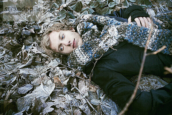Young man dressed with a thick scarf laying down between icy leaves