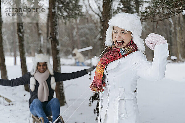 Glückliche Frau lässt ihre Muskeln spielen  während ein Mann auf einem Schlitten im Schnee sitzt