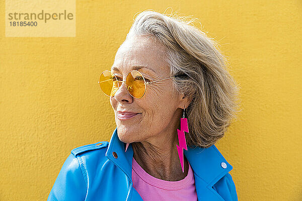 Nachdenkliche Frau mit Sonnenbrille vor gelber Wand