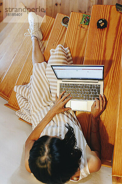 Frau sitzt mit Laptop auf der Treppe zu Hause