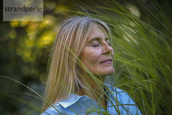 Frau mit geschlossenen Augen steht neben Pflanze im Garten